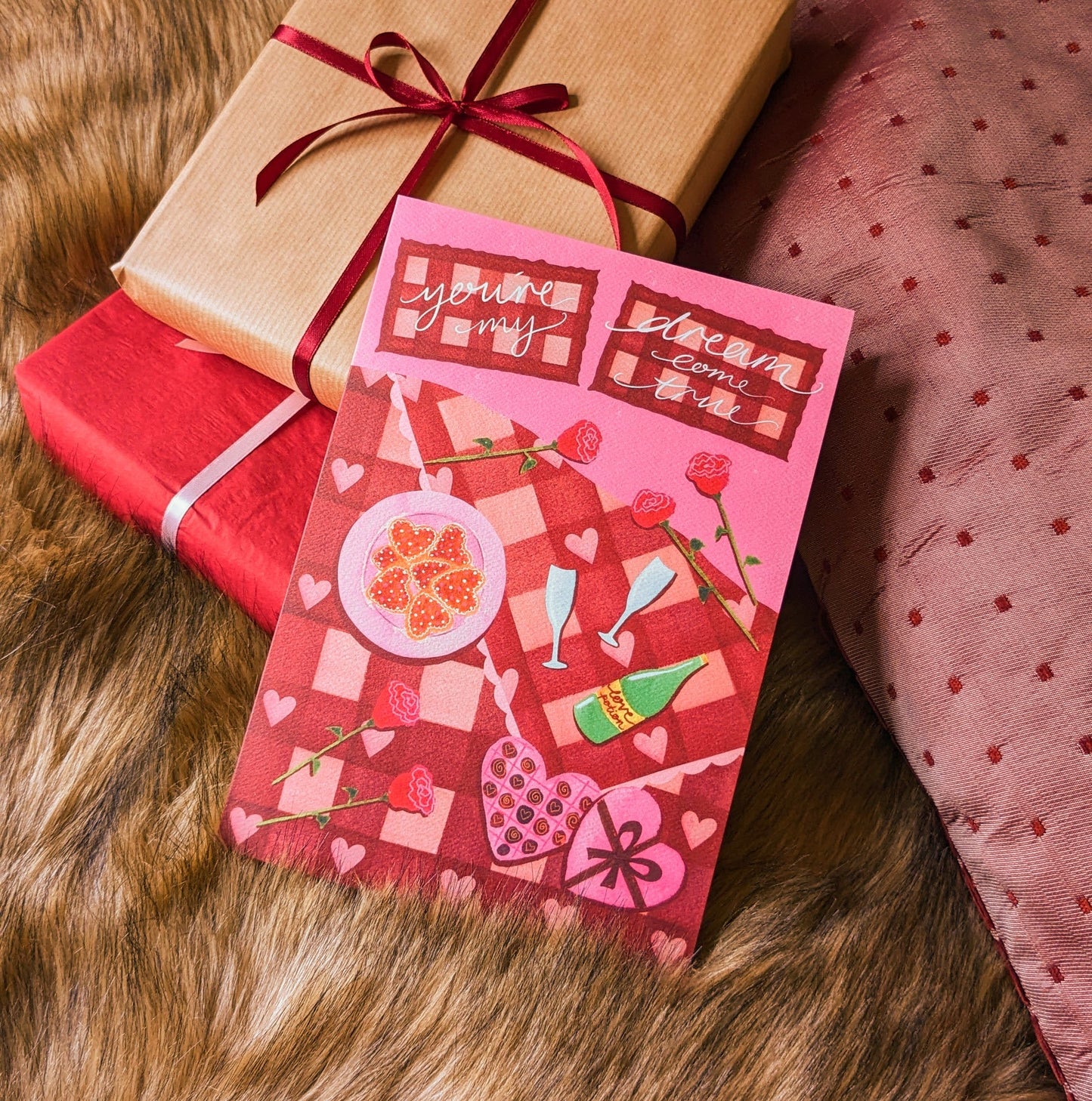 You're My Dream Come True, romantic bed spread greetings card. Featuring a pink and read quilted, double bed covered in roses, cookies, chocolates and a love potion. Perfect for Valentine's Day, anniversaries, engagements, celebrating love, girlfriends and boyfriends. A5 is size and printed on premium quality 300gsm card stock. Designed by luxury gifts and stationery brand, Bella & The Moon.