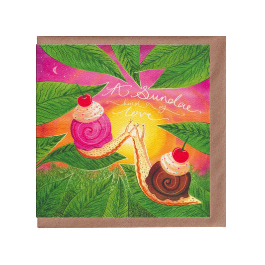 A Sundae Kind Of Love, Valentine's greetings card featuring a vibrant, romantic illustration of two snails with ice-cream and cherries on their shells, kissing in front of a sunset. Displayed standing next to an ice-cream sundae and biscuits on a wooden table outside. 14cm x 14cm, square in size and printed on premium quality 300gsm card stock. Designed by luxury gifts and stationery brand, Bella & The Moon
