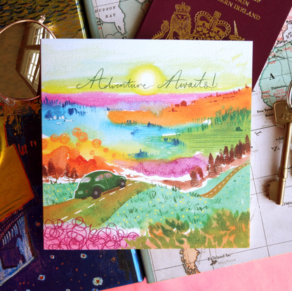 Adventure Awaits, traveller greetings card featuring a vibrant artistic landscape and a retro car. Displayed on a table with sunglasses, a passport, keys and a map. Perfect for travellers, backpackers, new drivers and exciting events. 14 x 14cm, square in size and printed on premium quality 300gsm card stock. Designed by luxury gifts and stationery brand, Bella & The Moon.