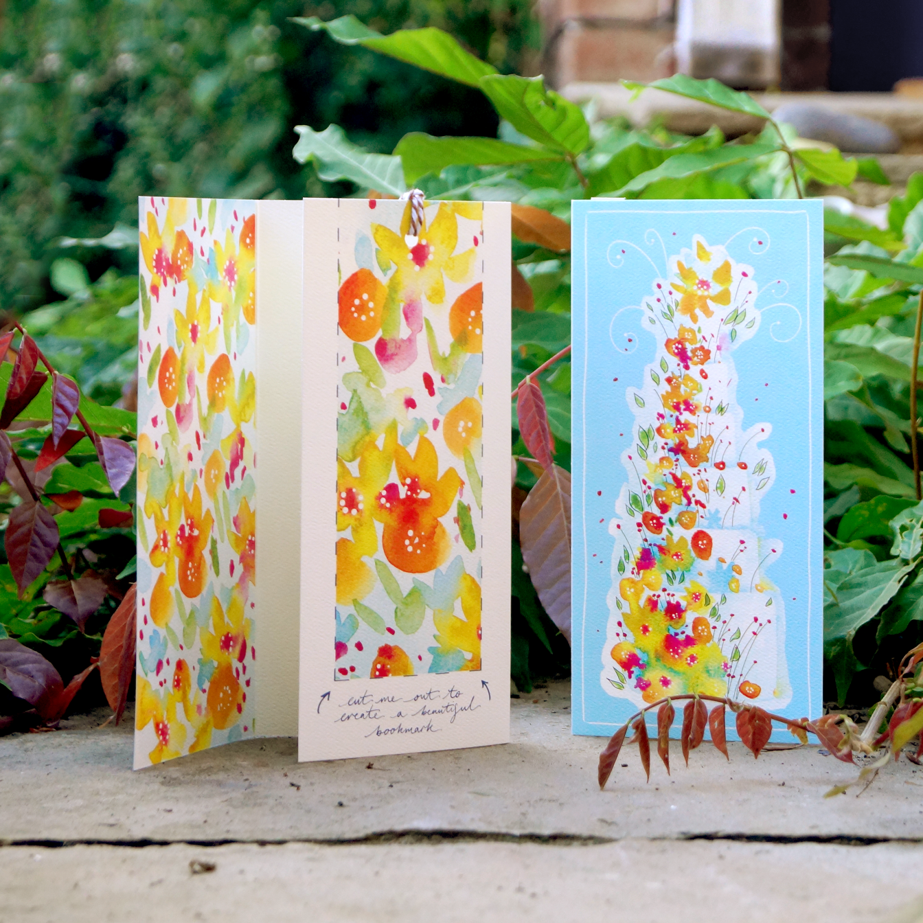 A floral birthday or wedding cake design on an extra special greeting card. The card includes a summery floral cut-out bookmark inside. Standing outside on stone amongst ivy. DL in size. Bella & The Moon gifts and stationery 