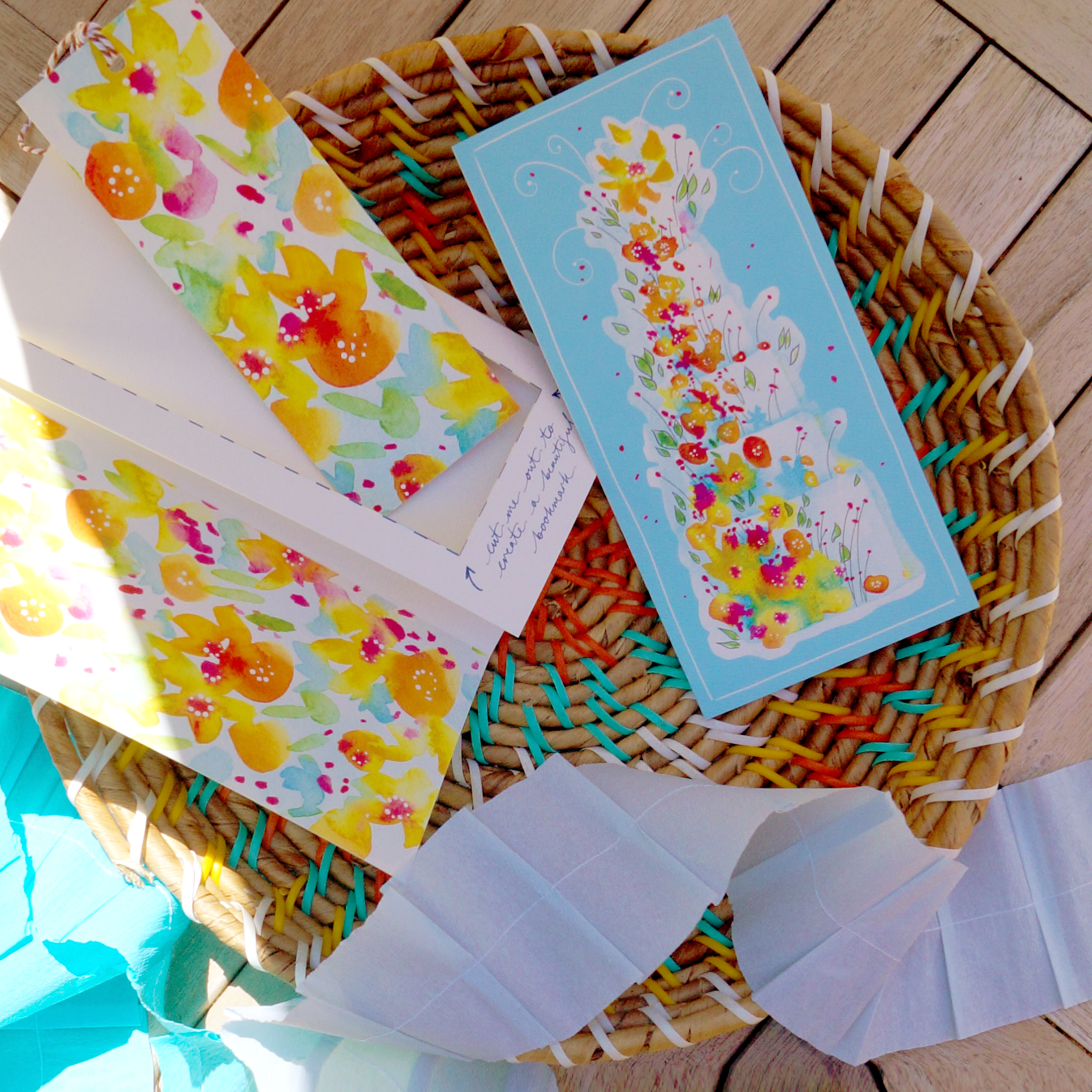 A floral birthday or wedding cake design on an extra special greeting card. The card includes a summery floral cut-out bookmark inside. Laying in a colourful fruit basket with decorative paper garlands. DL in size. Bella & The Moon gifts and stationery 