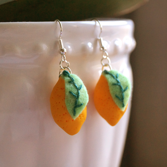 Handmade lemon-shaped earrings with green embroidered felt leaves, displayed on a white ceramic pot. Bella & The Moon gifts and stationery