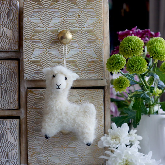 Handmade felt llama decoration displayed on a gold set of jewellery drawers next to green flowers. Approx 9cm x 5xm x 10cm Bella & The Moon (Handmade Gifts and Stationery)