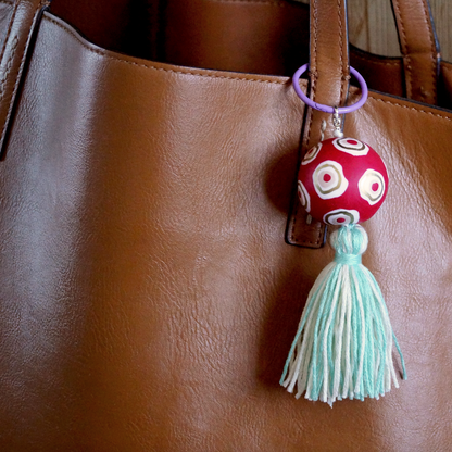 A handmade keyring featuring a red, gold and white handmade polymer bead and a handmade blue tassel. A keyring made to accessorise bags, keys and clothing. Bella & The Moon gifts and stationery