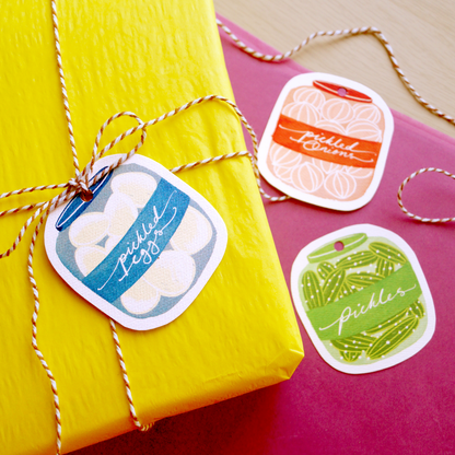 A photo of cut-out, jars-of-pickles gift tags tied to a colourful gift. Featuring pickled eggs, pickled gherkins and pickled onions. Present and gift wrapping. Unique and funny gifting ideas. Bella & The Moon gift and stationery