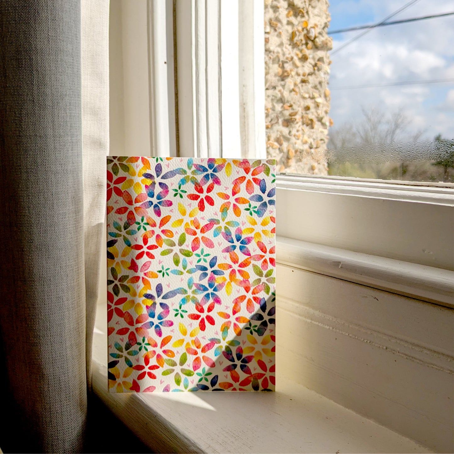 This rainbow blossom greetings card features a vibrant floral design with rainbow-coloured blossoms. Displayed on a sunny window cill. Perfect for birthdays, anniversaries, saying thank you,  spring celebrations or just because. A6 in size and printed on premium quality 300gsm card stock. Designed by luxury handmade gifts and stationery brand, Bella & The Moon.