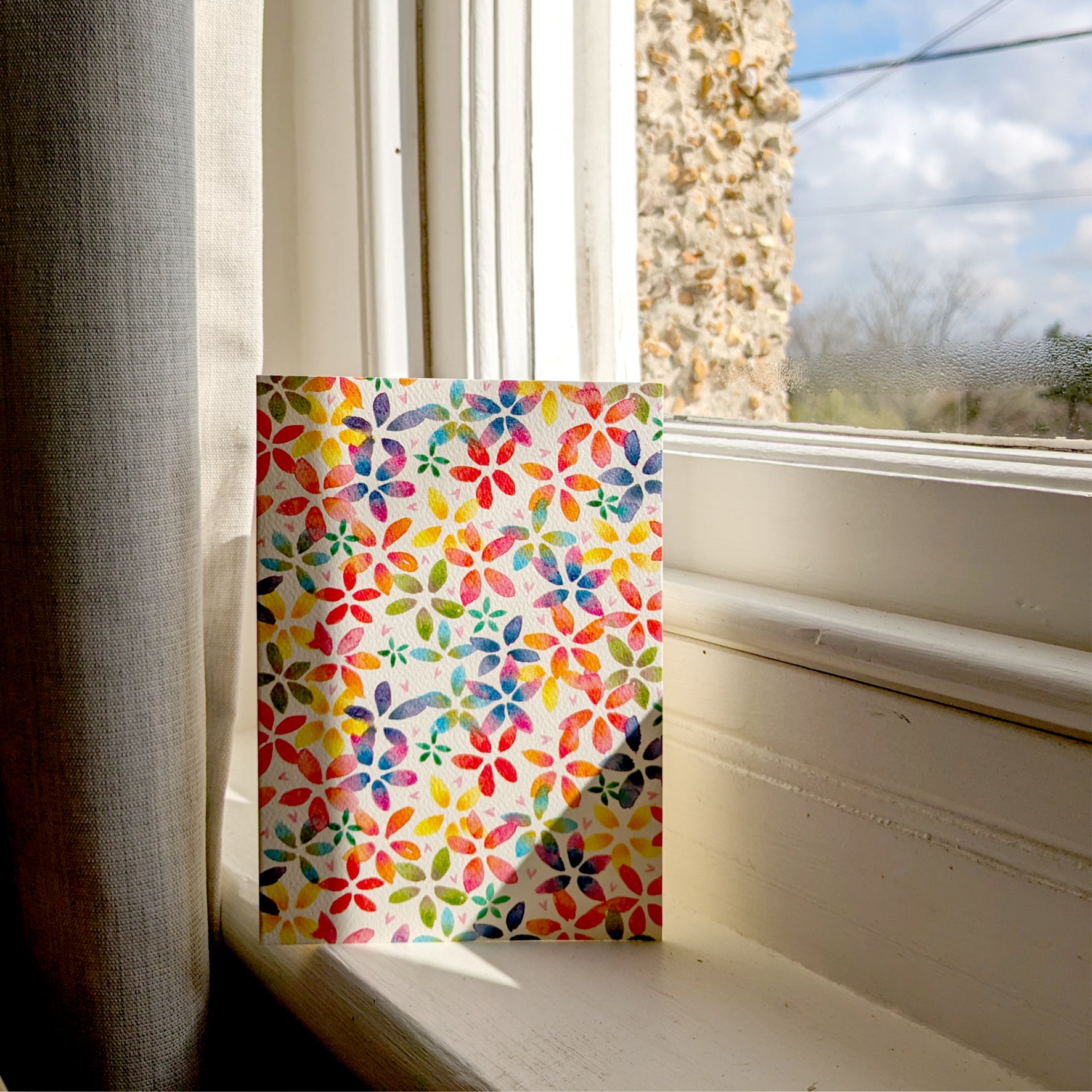 This rainbow blossom greetings card features a vibrant floral design with rainbow-coloured blossoms. Displayed on a sunny window cill. Perfect for birthdays, anniversaries, saying thank you,  spring celebrations or just because. A6 in size and printed on premium quality 300gsm card stock. Designed by luxury handmade gifts and stationery brand, Bella & The Moon.
