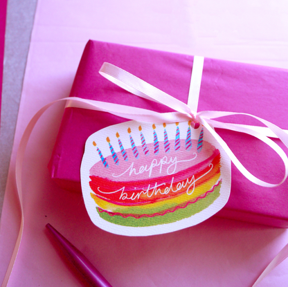 A rainbow, happy birthday cake gift tag tied onto a pink present. Present and gift wrapping. Unique and funny gifting ideas. Bella & The Moon gift and stationery