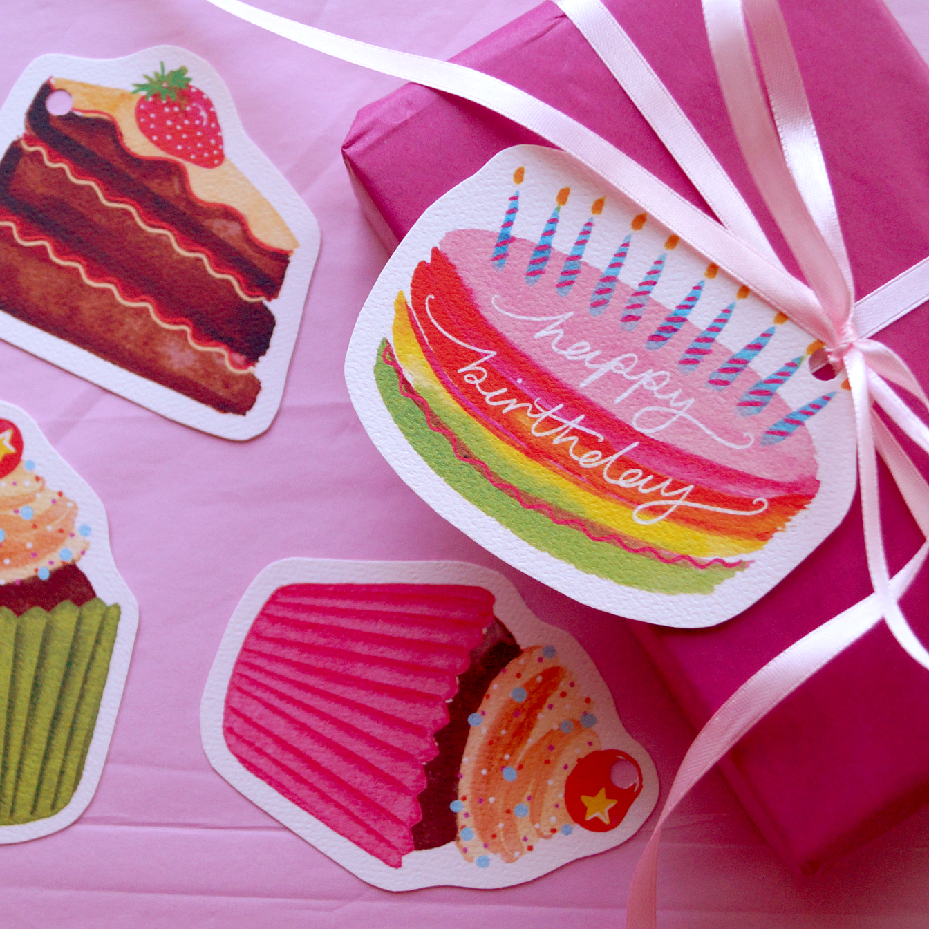 A photo of a rainbow, happy birthday cake gift tag tied to a pink present. Present and gift wrapping. Unique and funny gifting ideas. Bella & The Moon gift and stationery