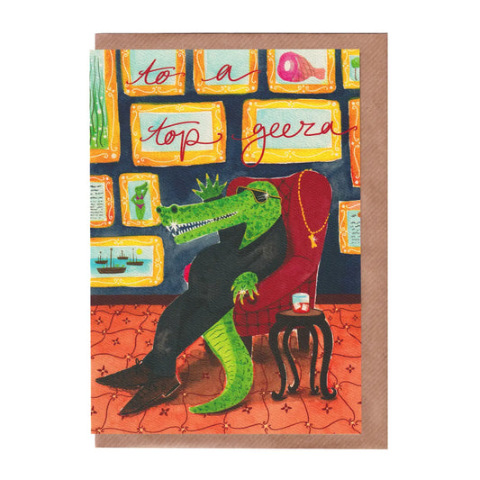 Greeting card with a crocodile lounging in a chair, surrounded by framed pictures, on a patterned background. A funny birthday, father's day or celebration card for men. A5 in size. Bella & The Moon gifts and stationery.