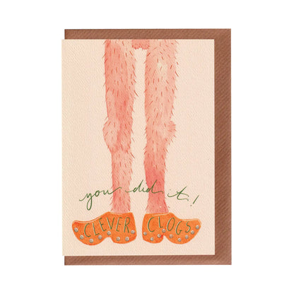 A funny, rude celebratory greeting card with illustration of traditional clogs and text saying 'you did it! clever clogs', on a white background. Celebration, graduation or achievement card. A6 in size. Bella & The Moon gifts and stationery.